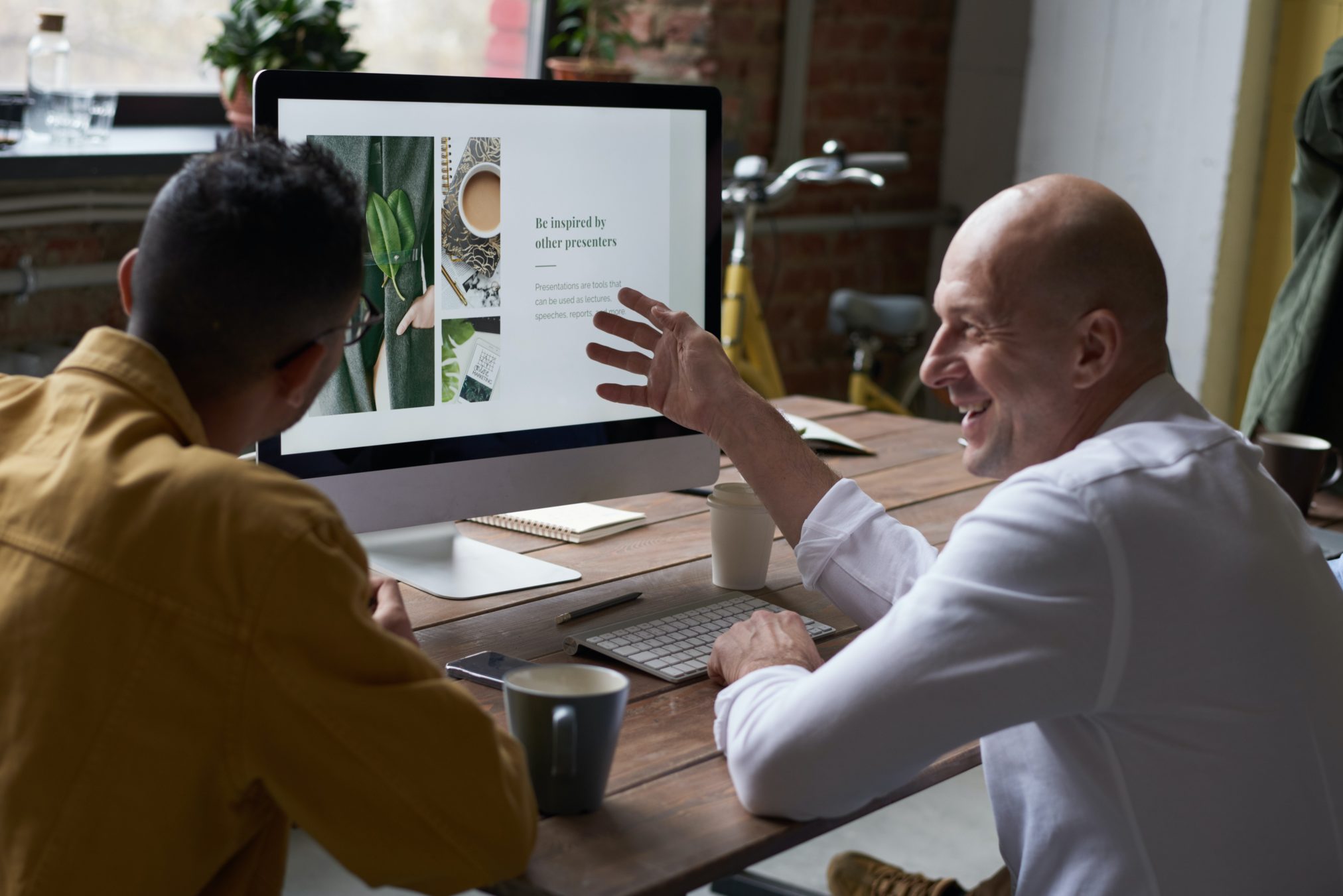 Two men working on a table looking at a computer and smiling